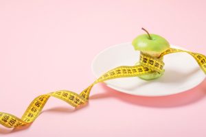 Apple core with measuring tape in place of the waist on a white plate on a pink background. Diet, weigh loss, starvation, fitness concept.